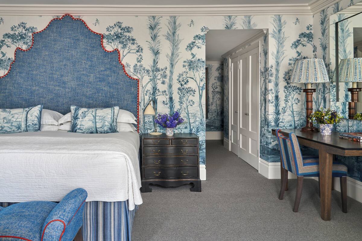 A bedroom with a large bed, a dresser, a desk with a lamp, and a chair.