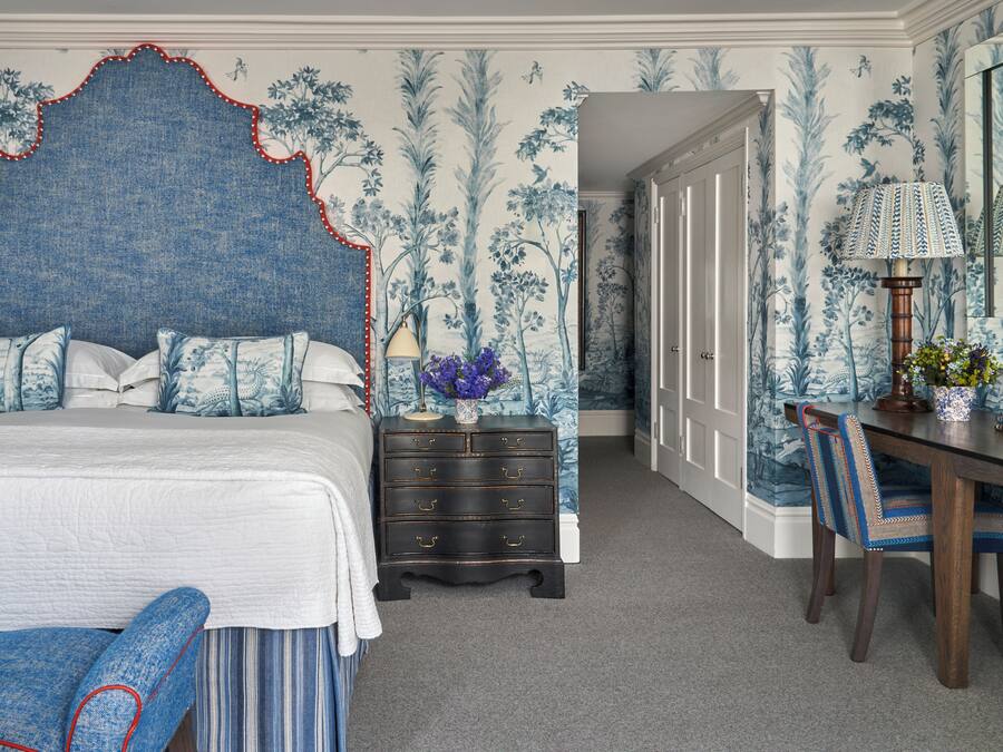 Quarto com cama grande, cômoda, escrivaninha com luminária e uma cadeira.