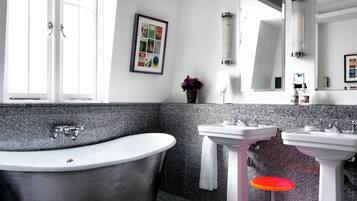 Une salle de bain moderne avec une baignoire sur pieds, deux vasques, un grand miroir et un tableau encadré au mur.