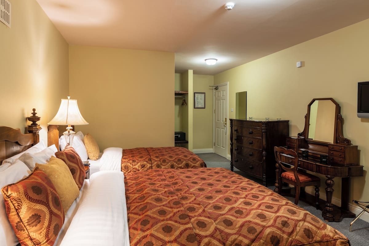 A hotel room with two beds, a dresser, a chair, and a TV.