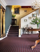 A grand staircase with ornate railings, a chandelier, and a patterned carpet.