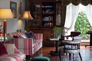 A cozy living room with a striped sofa, a red armchair, a wooden bookshelf, and a window with curtains.