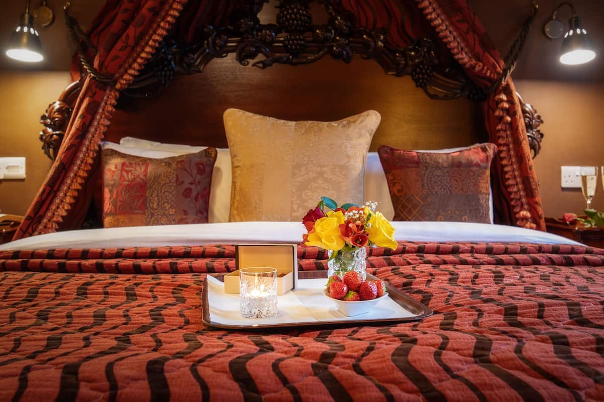 A bed with a canopy, a tray with a candle, a vase with flowers, and a tray with strawberries.