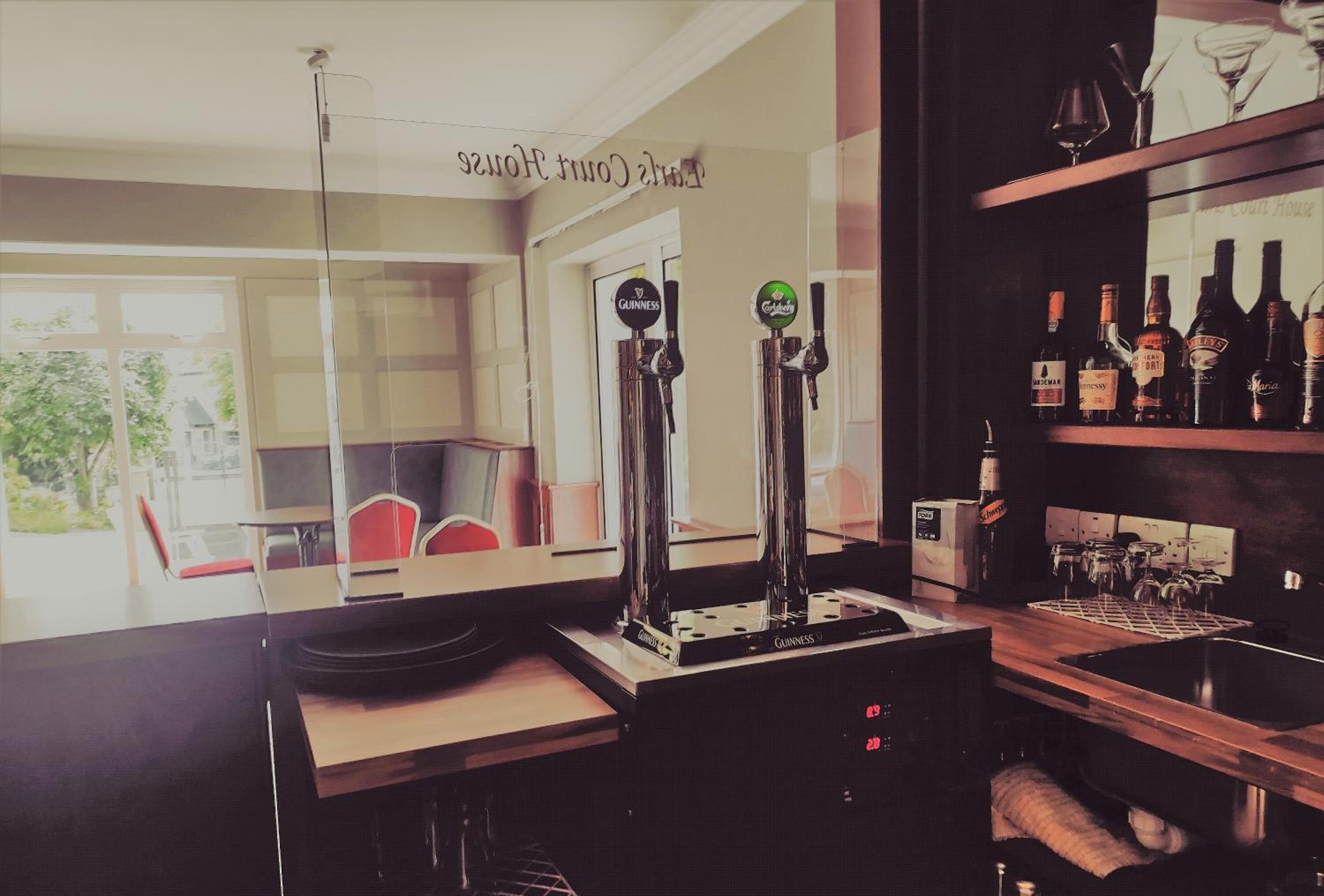 Una zona de bar con dos grifos de Guinness, una estantería con varias botellas y vistas al exterior.