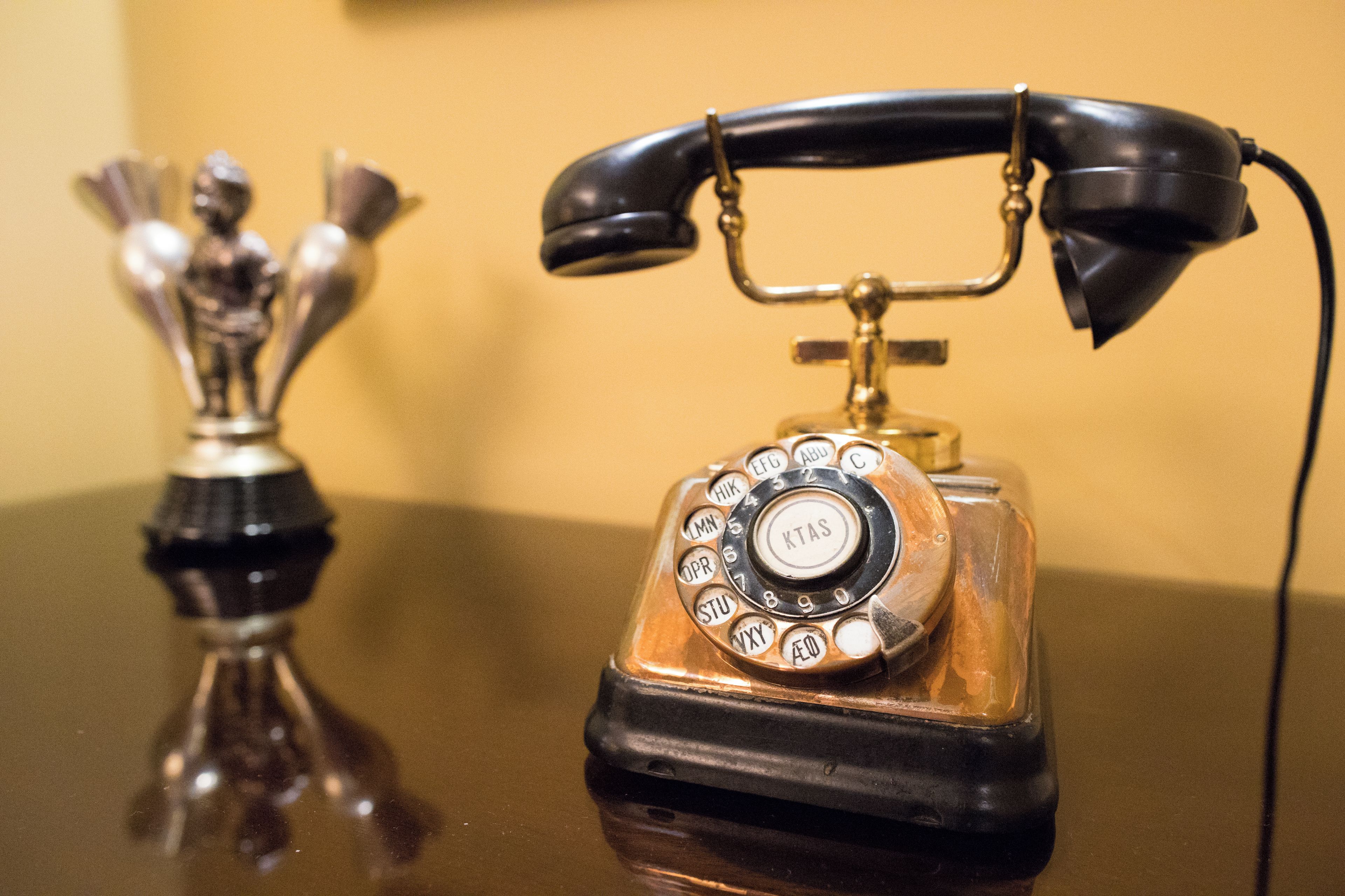 Ein altes Wählscheibentelefon mit schwarzem Hörer und metallischem Fuß, platziert auf einer spiegelnden Oberfläche.