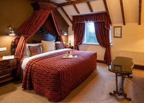 A bedroom with a four-poster bed, a nightstand, a bedside table, a window with curtains, and a radiator. - Earls Court House Hotel (Killarney)