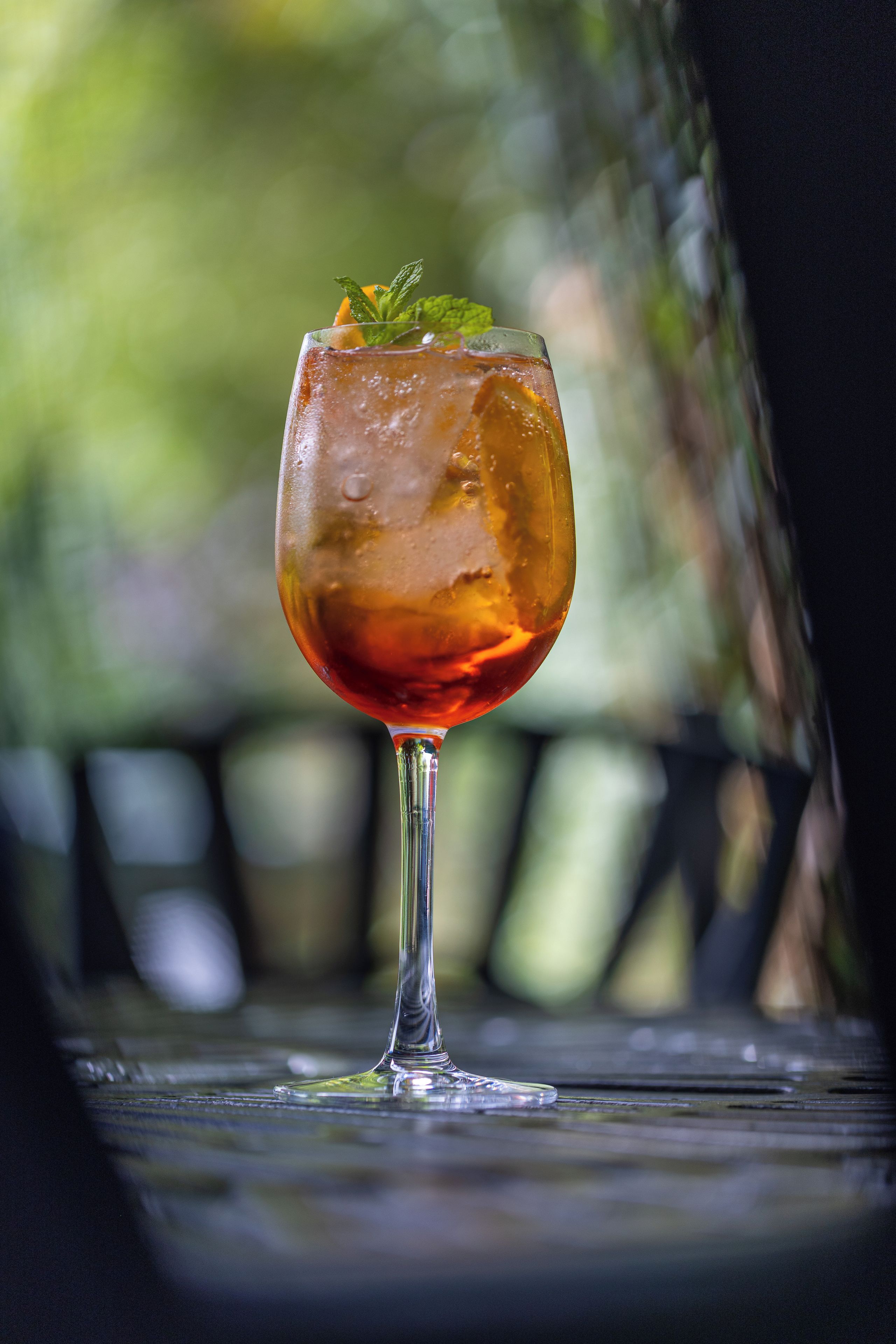 Ein Glas mit roter Flüssigkeit, Eiswürfeln und einem Minzblatt auf einer Metalloberfläche.