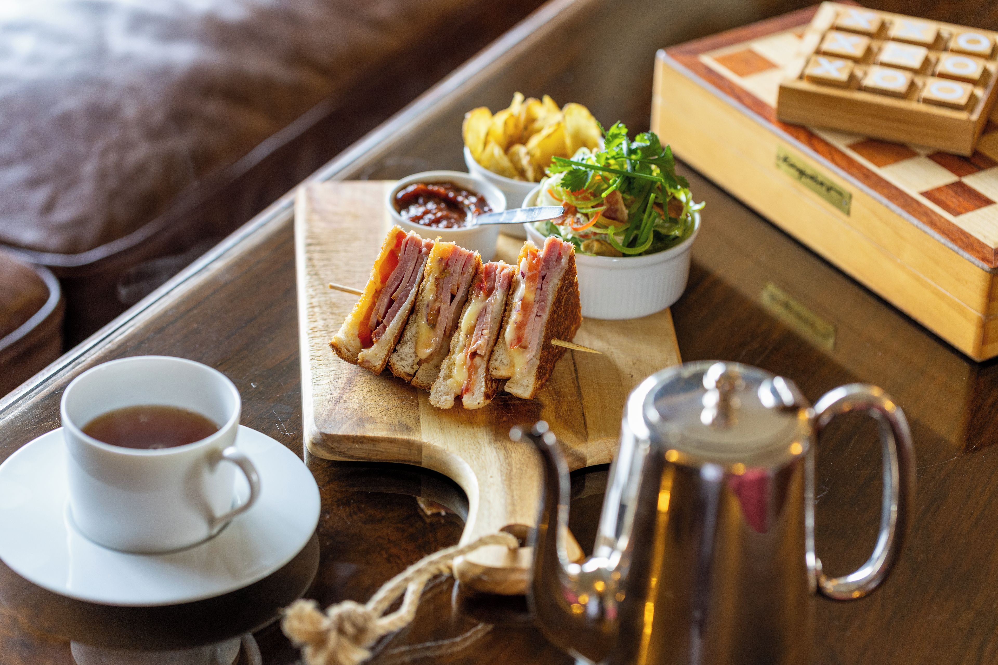 A tray with a sandwich, a cup of tea, a bowl of salad, and a chessboard.