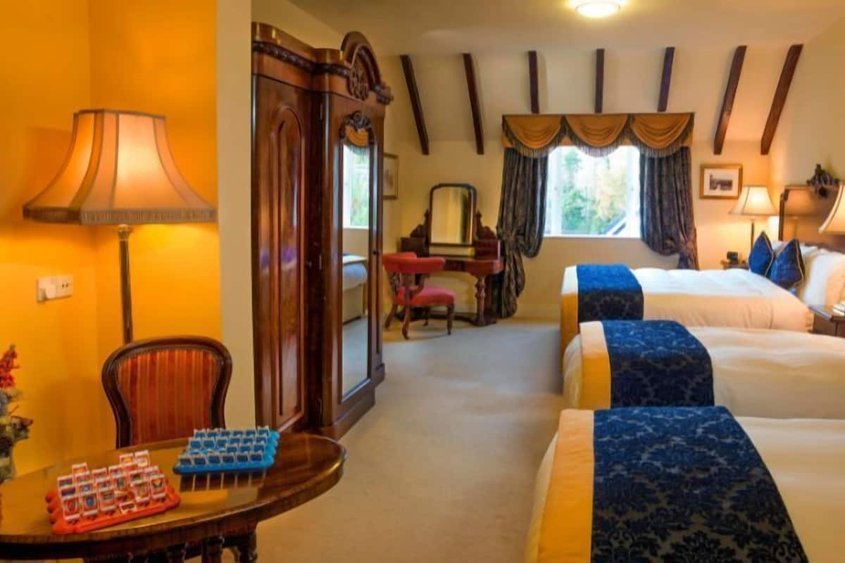 A hotel room with two beds, a desk, a chair, a mirror, and a window with curtains.