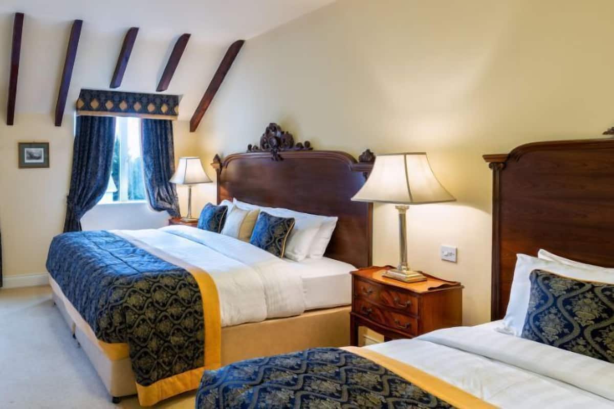 A hotel room with two beds, a wooden headboard, a nightstand, and a window with curtains.