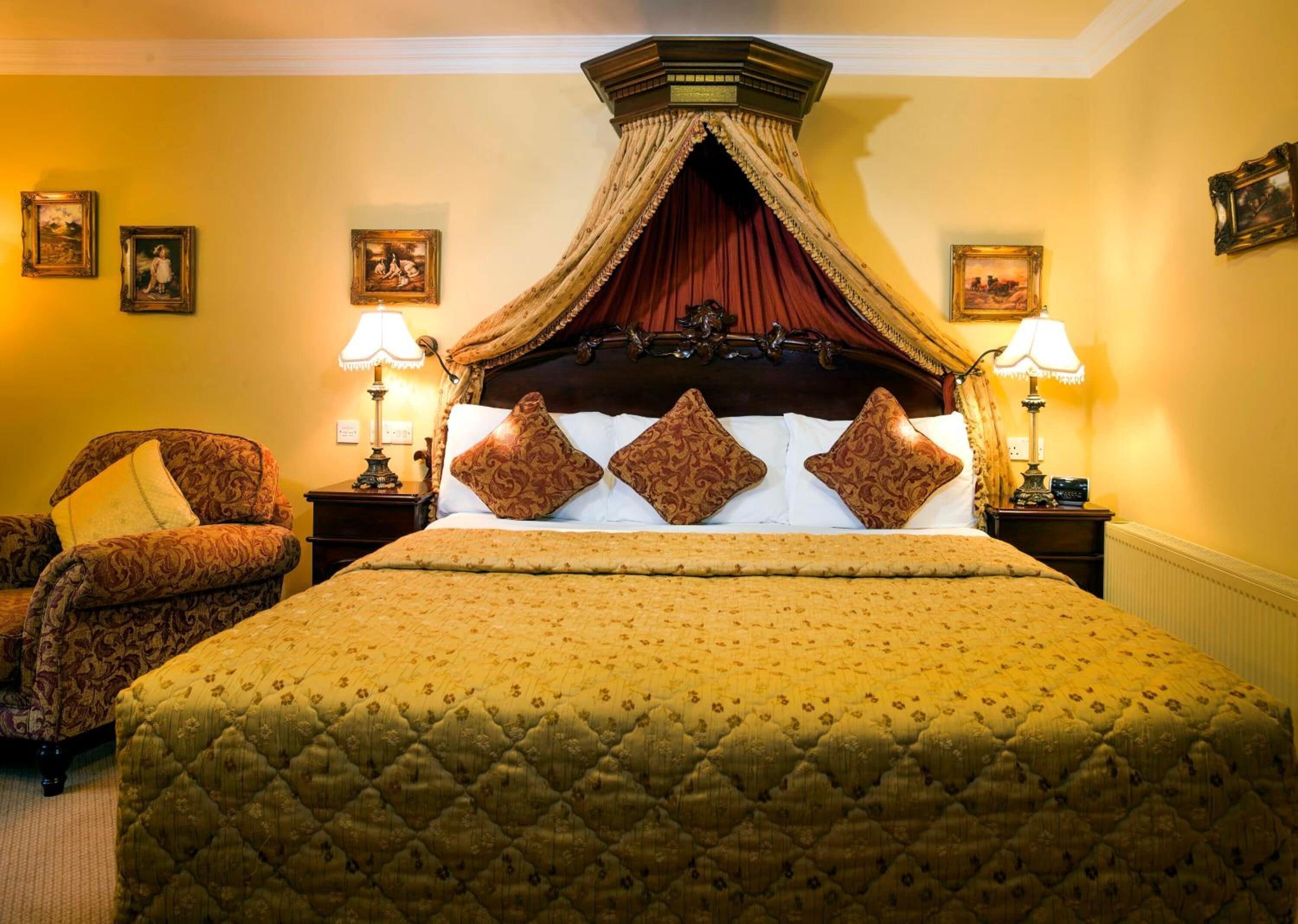 Un dormitorio con una cama grande, dos mesitas de noche con lámparas, una silla y cuadros enmarcados en las paredes, además de un dosel decorativo.