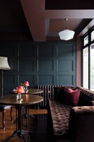 A room with a dark wooden floor, a round table with two lamps, a cushioned bench, and a radiator.