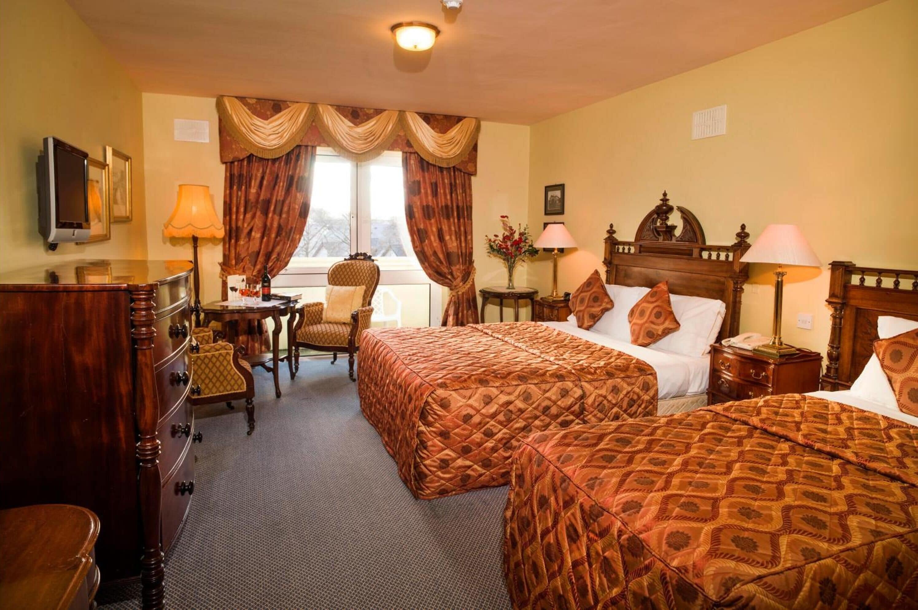 A hotel room with two beds, a desk, a chair, a TV, and a window with curtains.