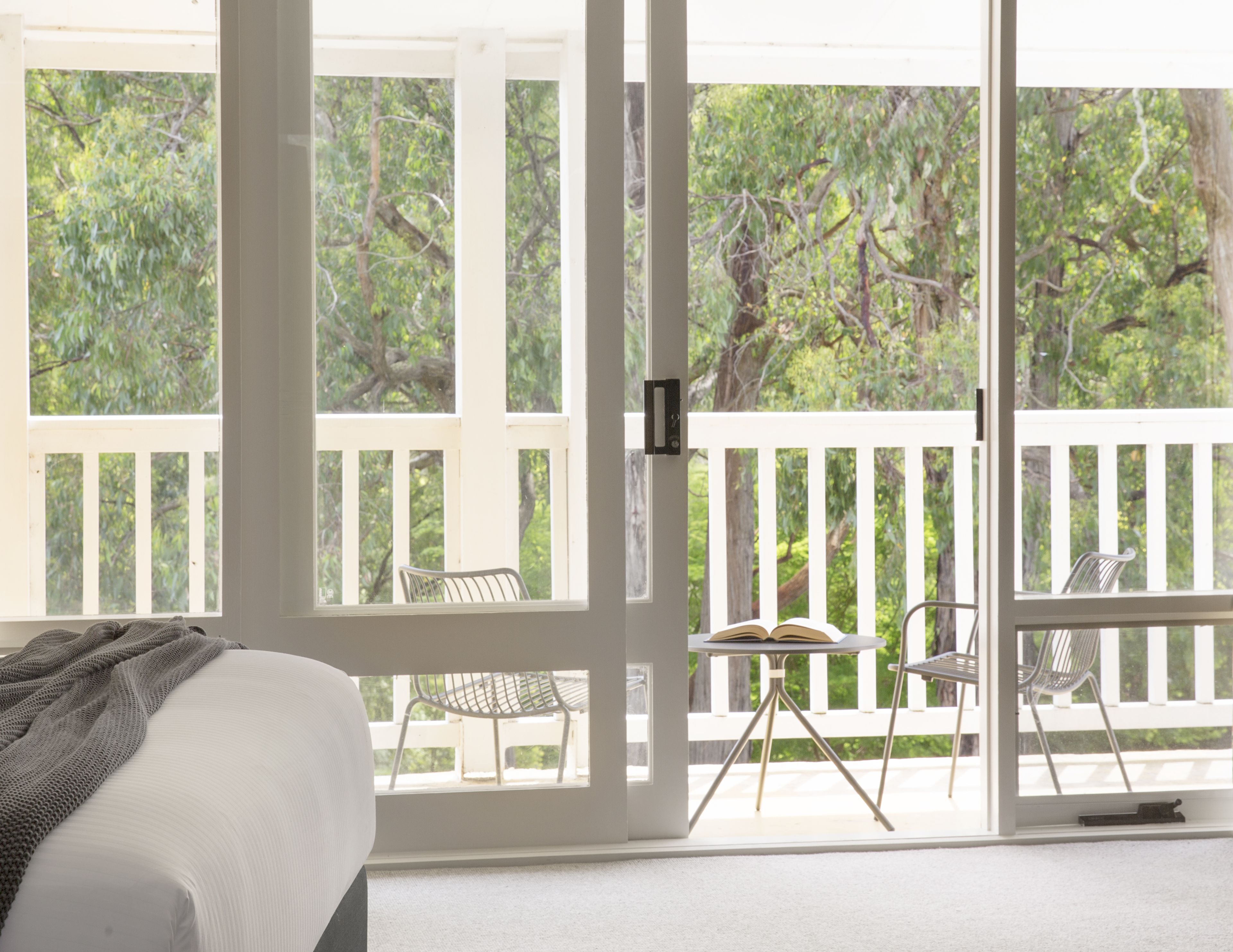 Una habitación con cama, ventana y balcón con sillas y una mesa.