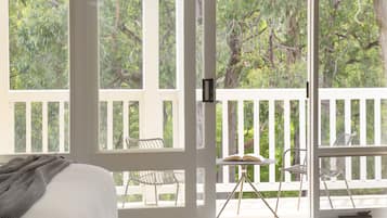 Una habitación con cama, ventana y balcón con sillas y una mesa.