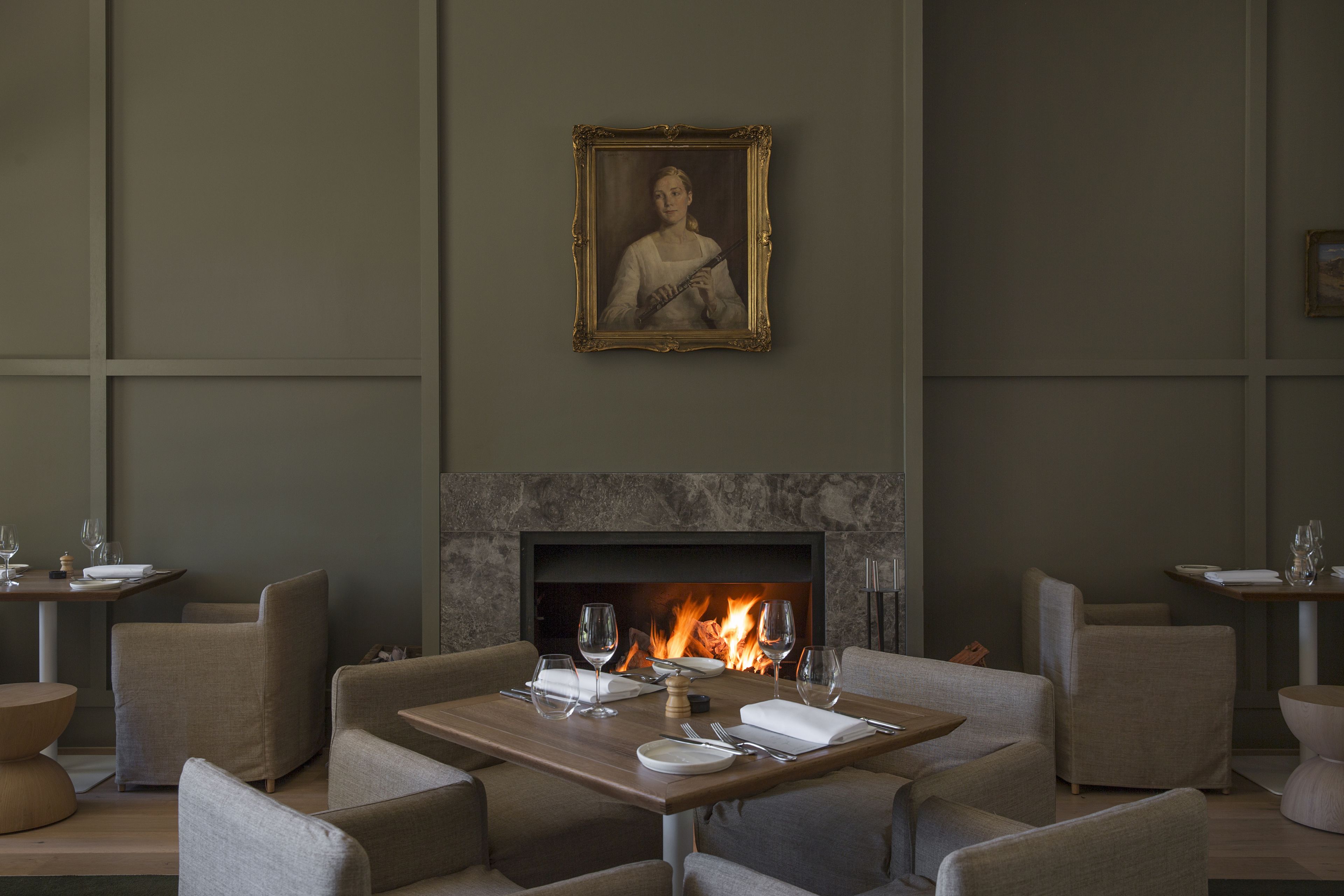 A dining area with a fireplace, a framed portrait, and a table set for two.