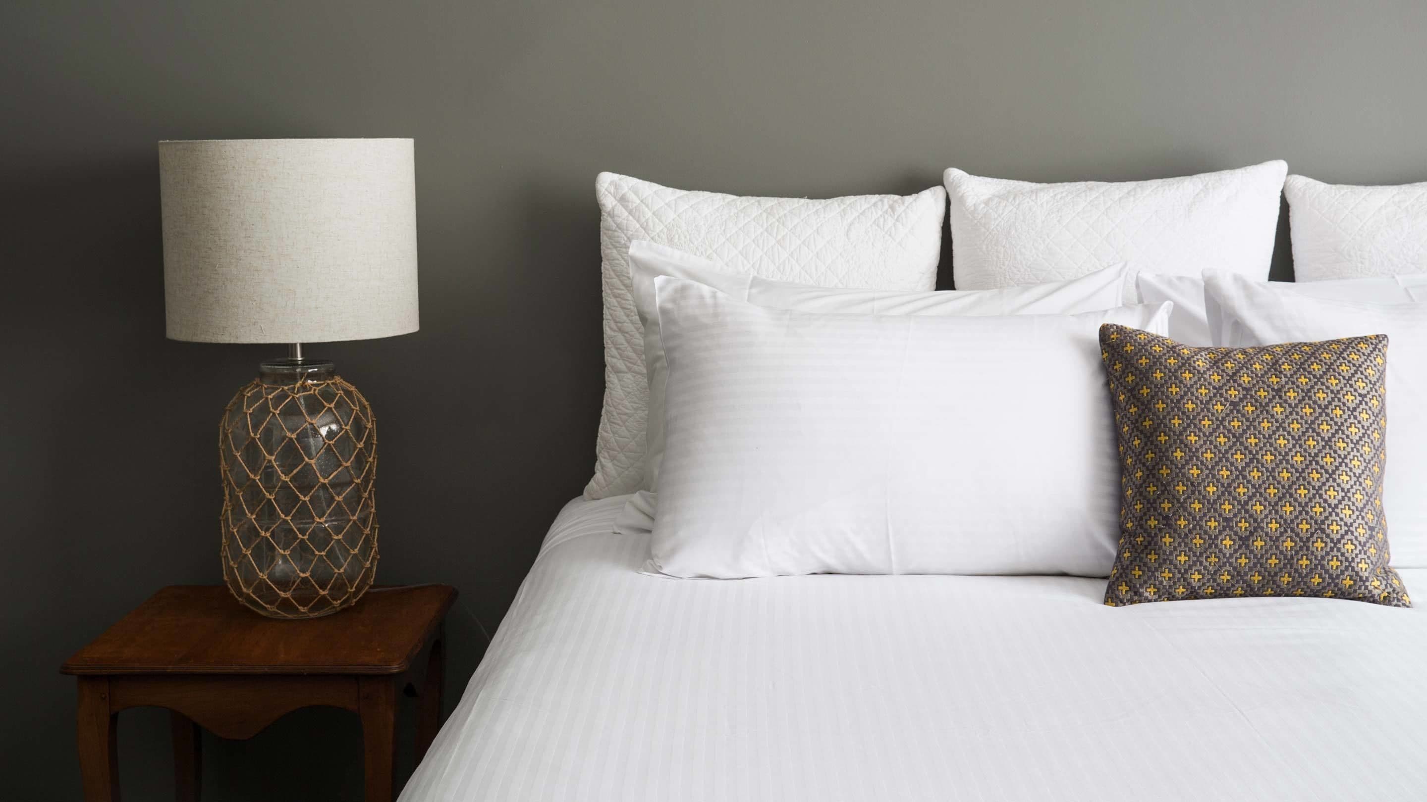 A neatly made bed with white linens, a patterned pillow, and a lamp on a wooden nightstand.