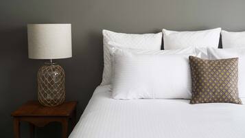 A neatly made bed with white linens, a patterned pillow, and a lamp on a wooden nightstand.