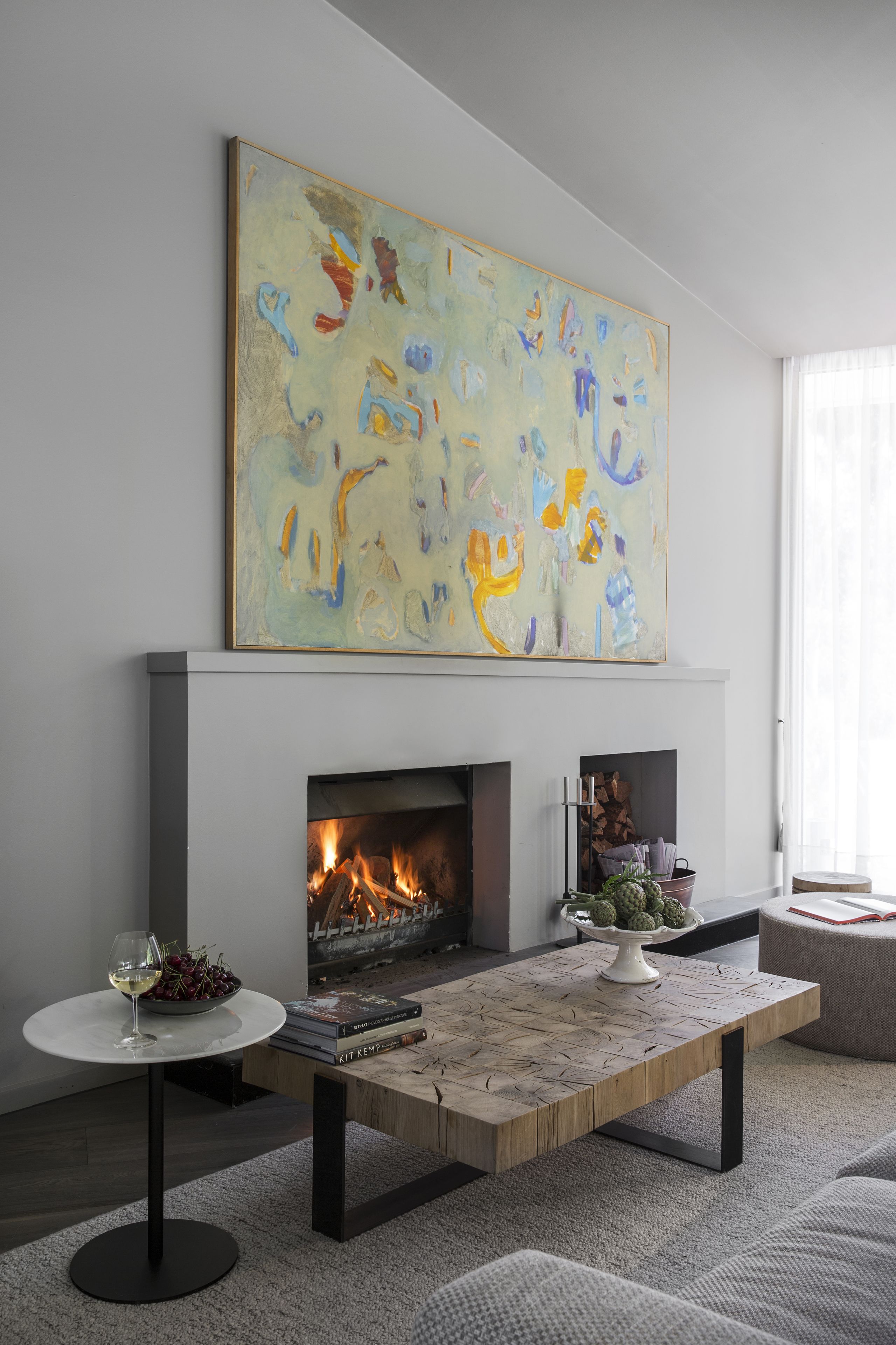 A modern living room with a fireplace, abstract art, a round table with a glass, and a coffee table.