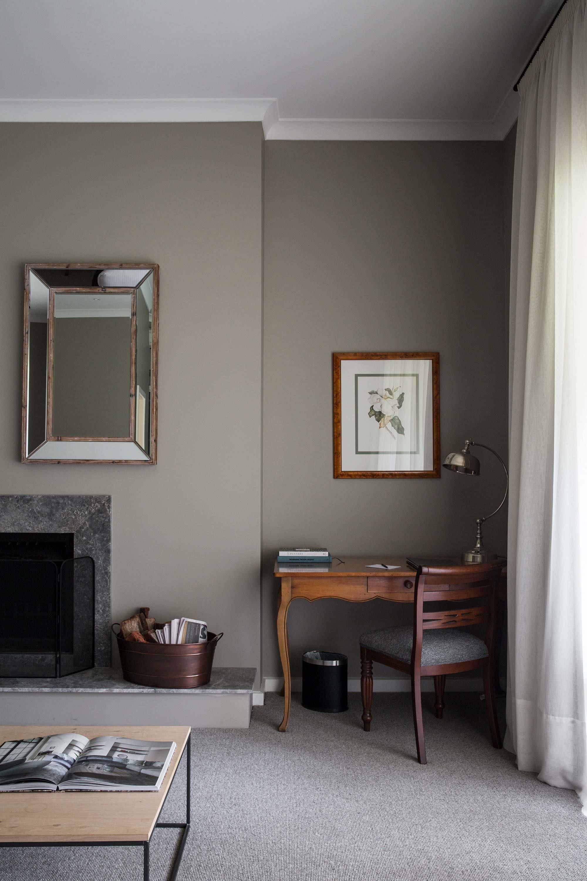 A living room with a fireplace, a desk with a chair, a mirror, and a framed picture on the wall.