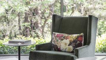 A modern living room with a green armchair, a round ottoman, and a small table with a glass of wine and a book.