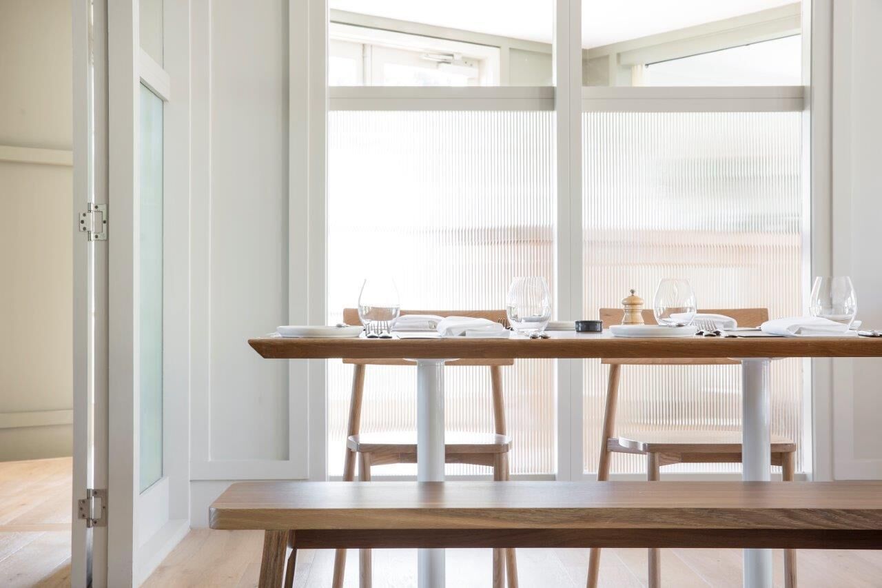 A dining area with a wooden table set for two, white chairs, and a bench.