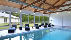 Piscina con sillones de descanso y vista a una casa y jardín.