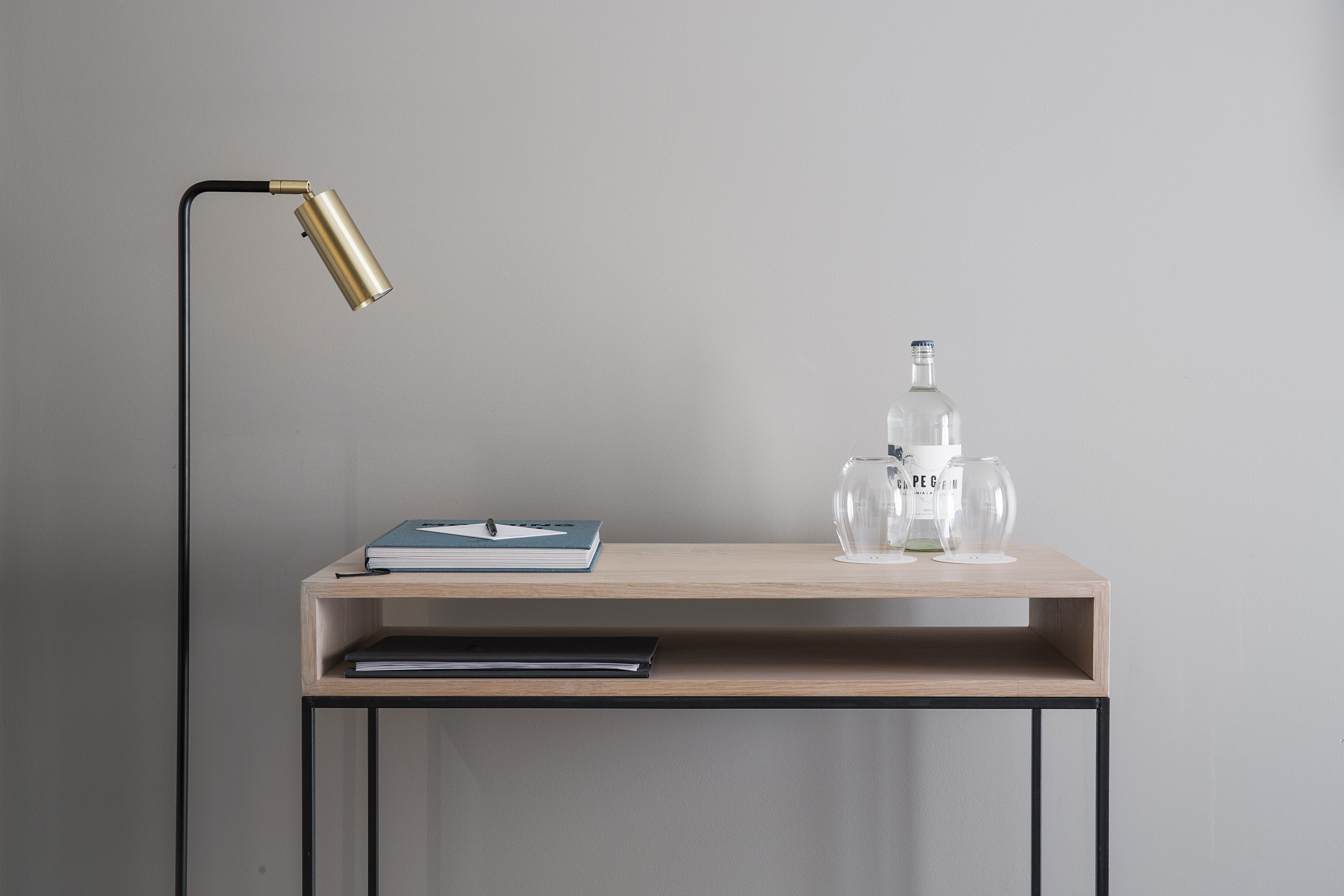 A minimalist desk with a lamp, a book, a glass bottle, and a glass.