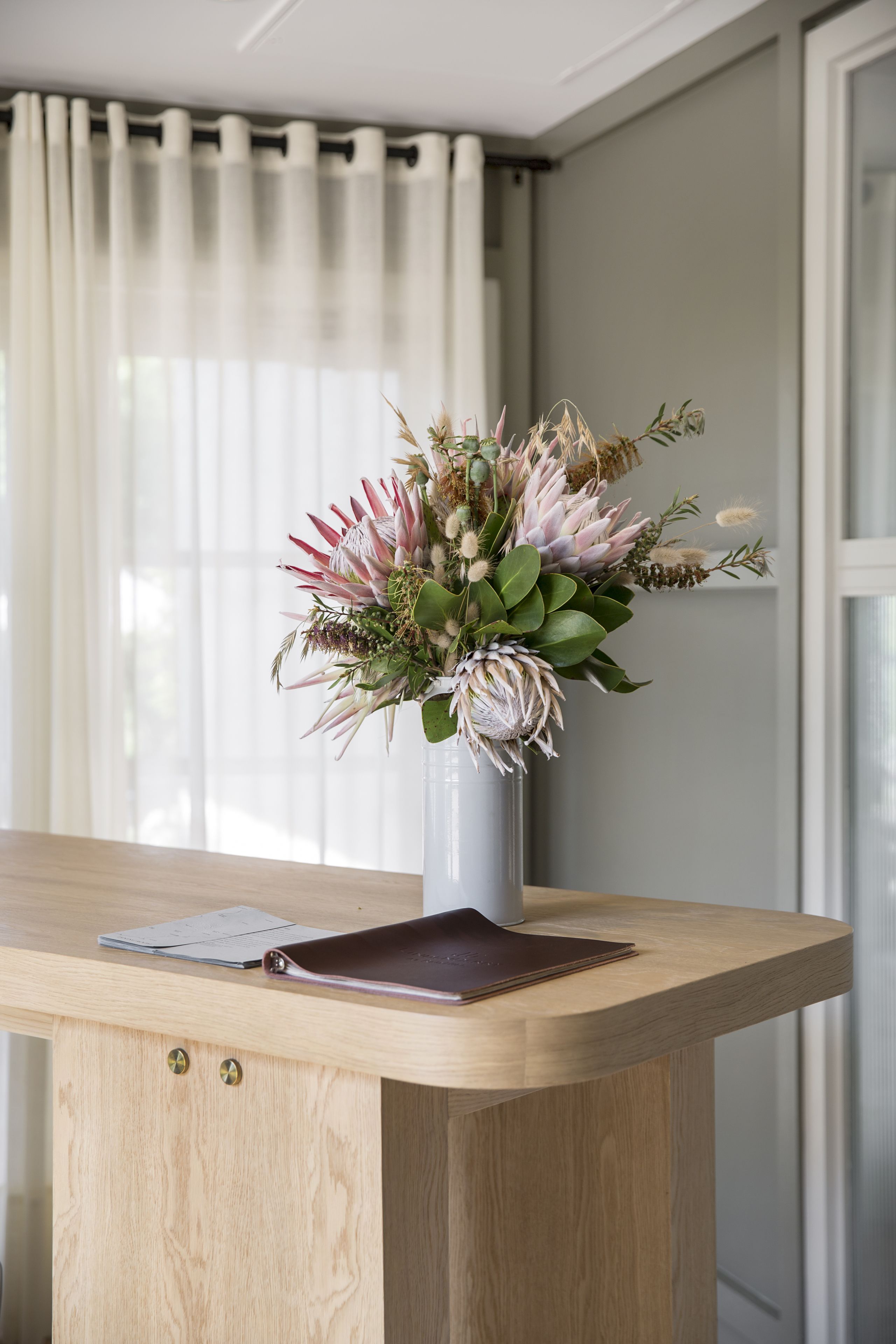 Una scrivania in legno con un vaso di fiori, un quaderno e una custodia in pelle.