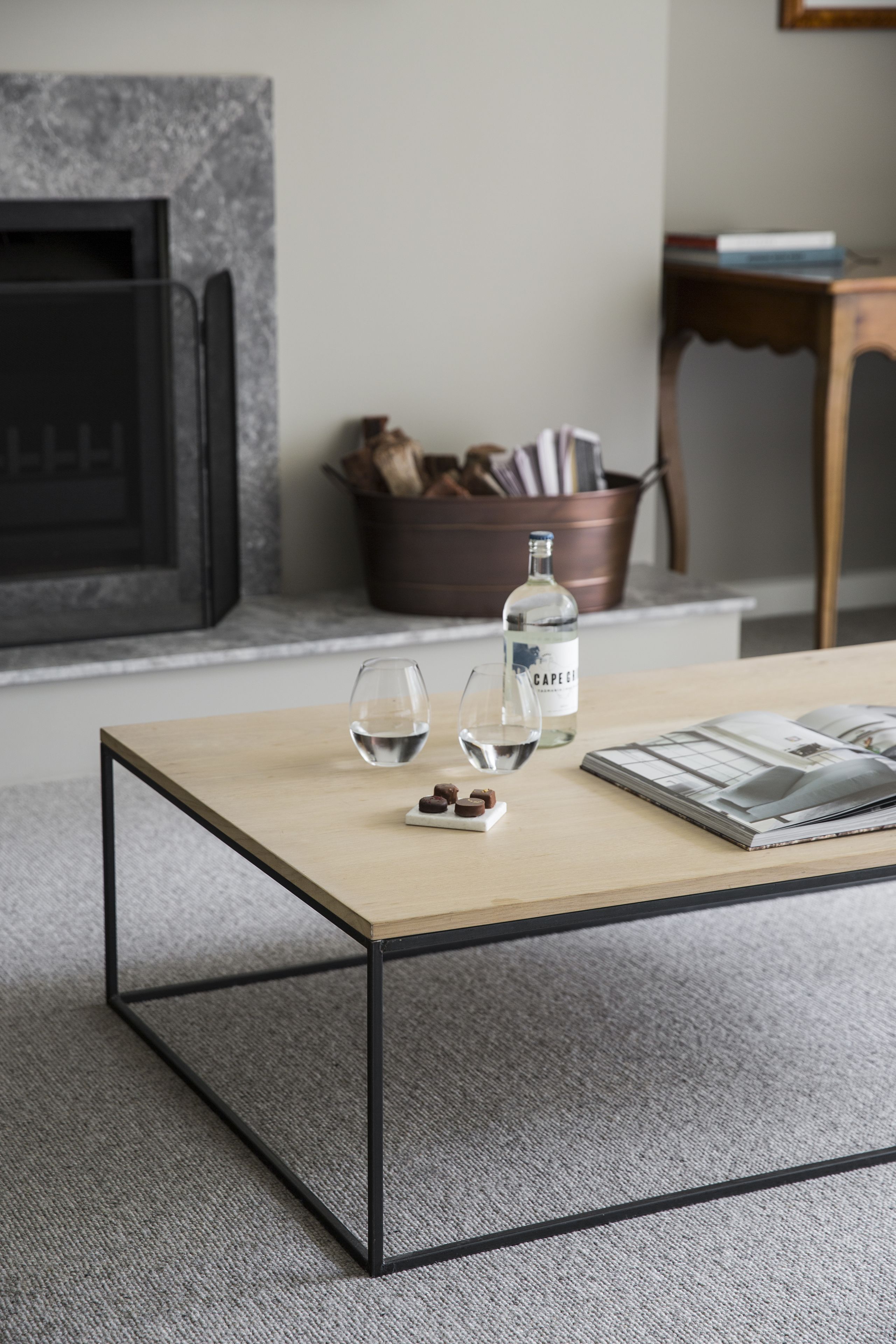 Una sala de estar moderna con una mesa de centro de madera, dos copas de vino, una botella de agua y una revista.