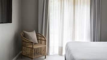 A bedroom with a bed, a wicker chair with a cushion, and sheer curtains.