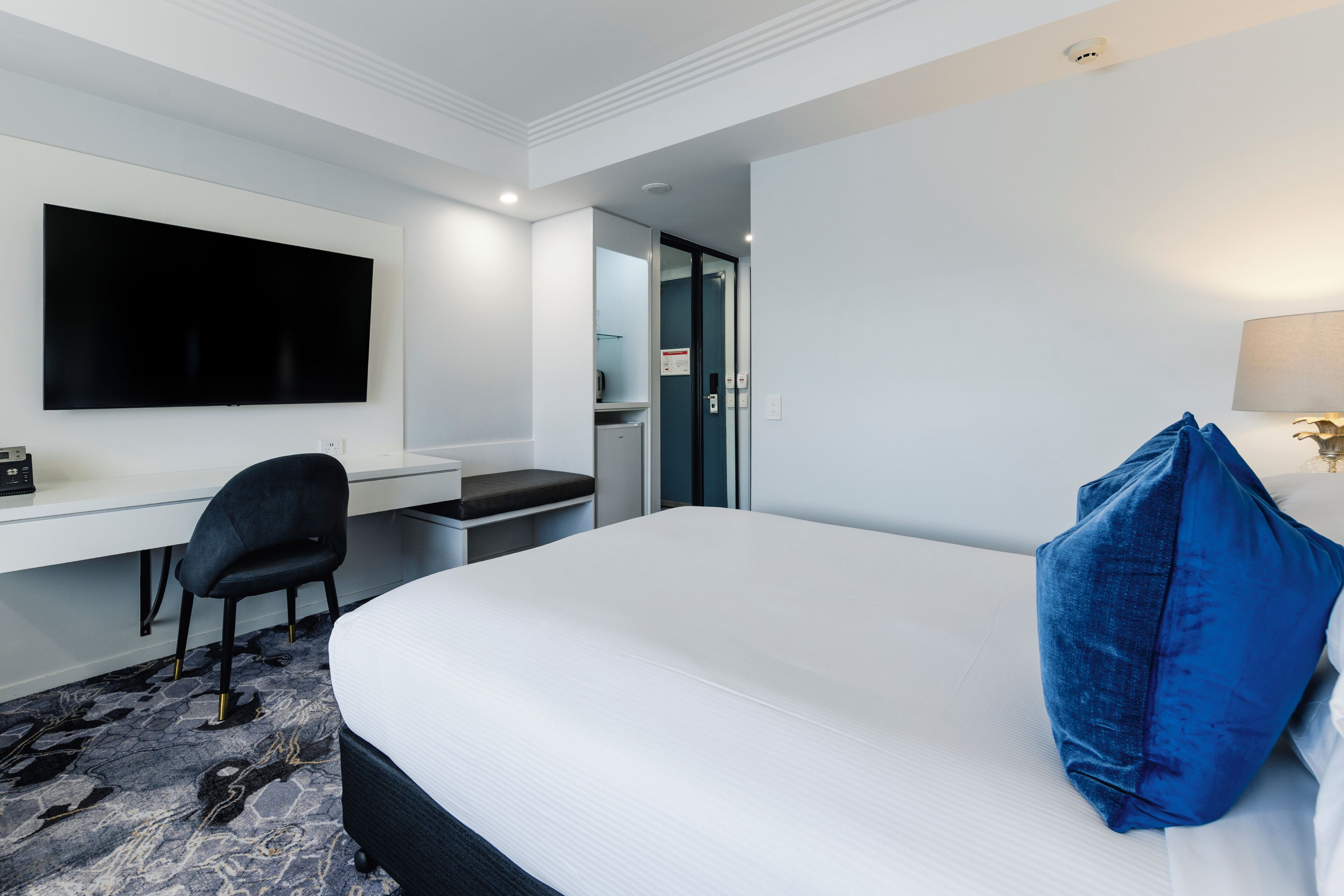 Habitación de hotel con una cama grande, un escritorio con una silla, un televisor de pantalla plana en la pared y una puerta que da a un baño.