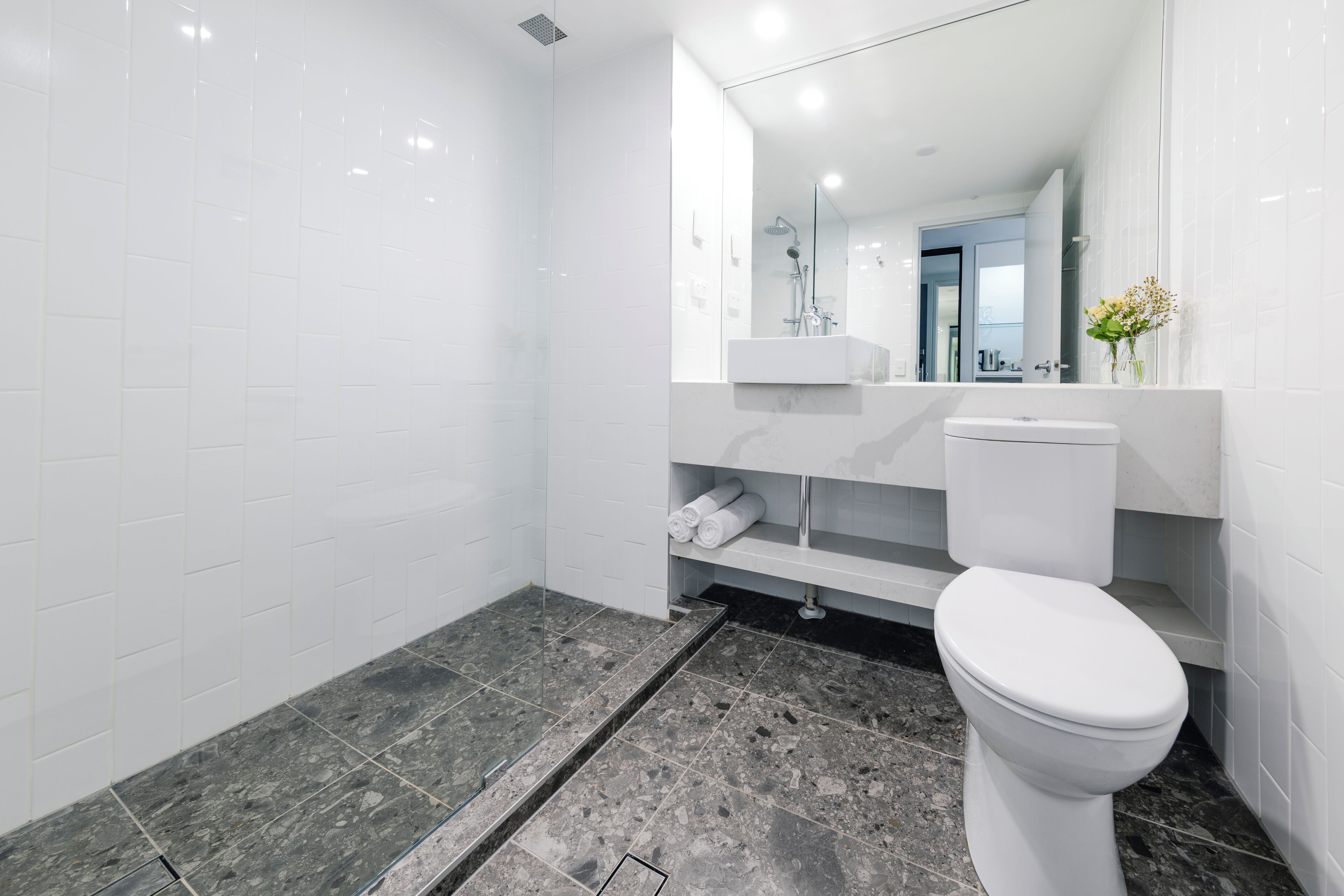 Un baño moderno con ducha de vidrio, inodoro blanco y encimera de mármol.