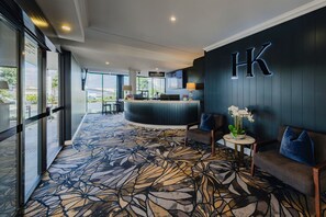 A hotel reception area with a reception desk, seating area, and a large window offering a view of the outdoors. - Hotel Kingsley (Hamilton)
