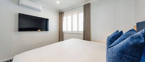 A hotel room with a bed, a flat-screen TV mounted on the wall, and a window with curtains.