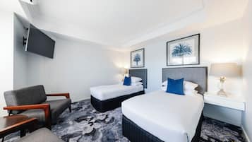 Ett hotellrum med en säng, två sängbord, en stol, en tv och två inramade tavlor på väggen.