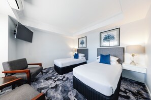 A hotel room with a bed, two bedside tables, a chair, a TV, and two framed pictures on the wall. - Hotel Kingsley (Hamilton)