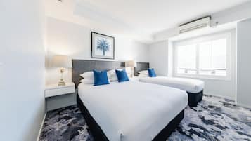 A hotel room with two beds, a framed picture on the wall, a window with blinds, and a patterned carpet.