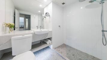 A modern bathroom with a toilet, two sinks, a shower, and a glass-enclosed shower area.