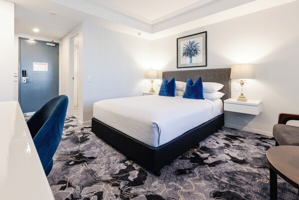 Una habitación de hotel con una cama grande, dos mesitas de noche con lámparas, una silla y una puerta.