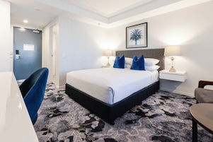 Una habitación de hotel con una cama grande, dos mesitas de noche con lámparas, una silla y una puerta.