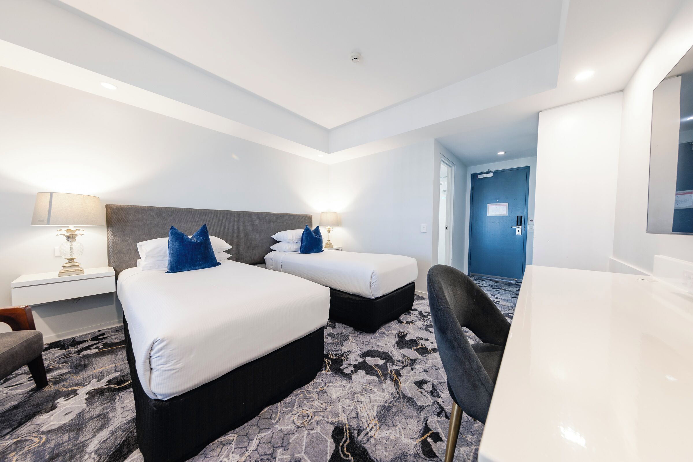 A hotel room with two beds, a desk, a chair, and a large mirror.