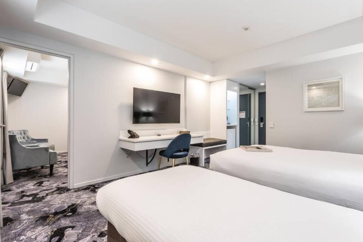 Habitación de hotel con dos camas, un escritorio, una silla, un televisor y un armario.