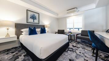 Une chambre d’hôtel avec un grand lit, deux tables de chevet, un bureau, une chaise et une fenêtre avec des stores.