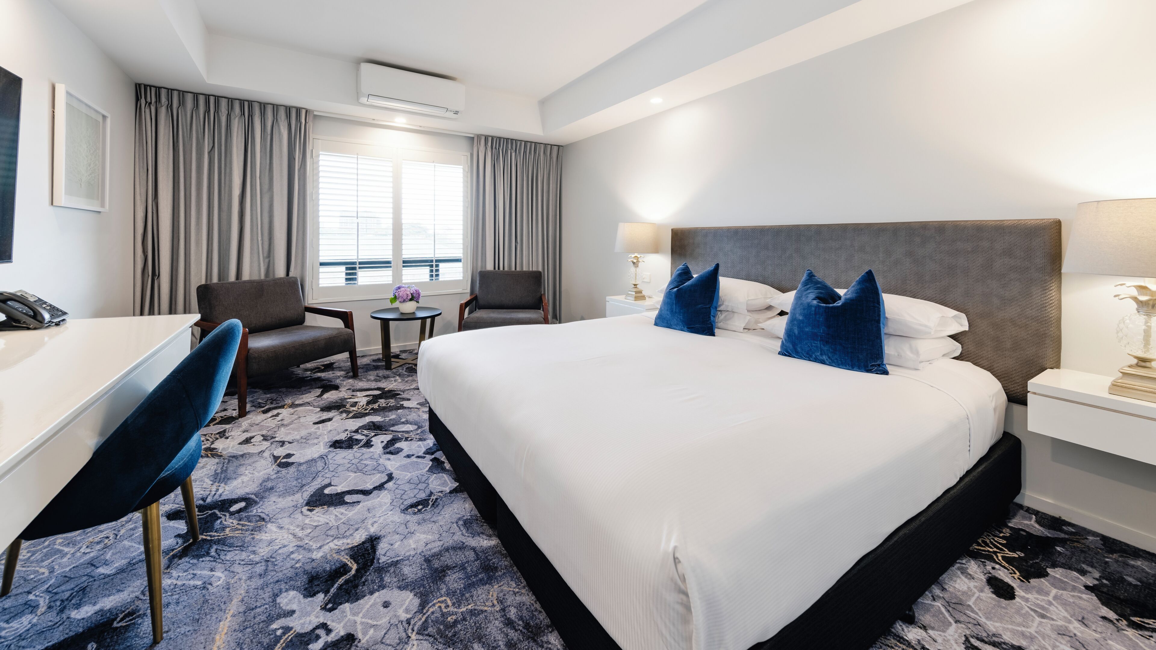 Une chambre d’hôtel avec un grand lit, un bureau, une chaise, une petite table et une fenêtre avec des rideaux.