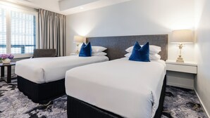 A hotel room with two beds, a nightstand, a lamp, and a window with curtains. - Hotel Kingsley (Hamilton)