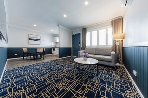 A hotel room with a dining area, a sofa, a coffee table, and a window with curtains. - Hotel Kingsley (Hamilton)