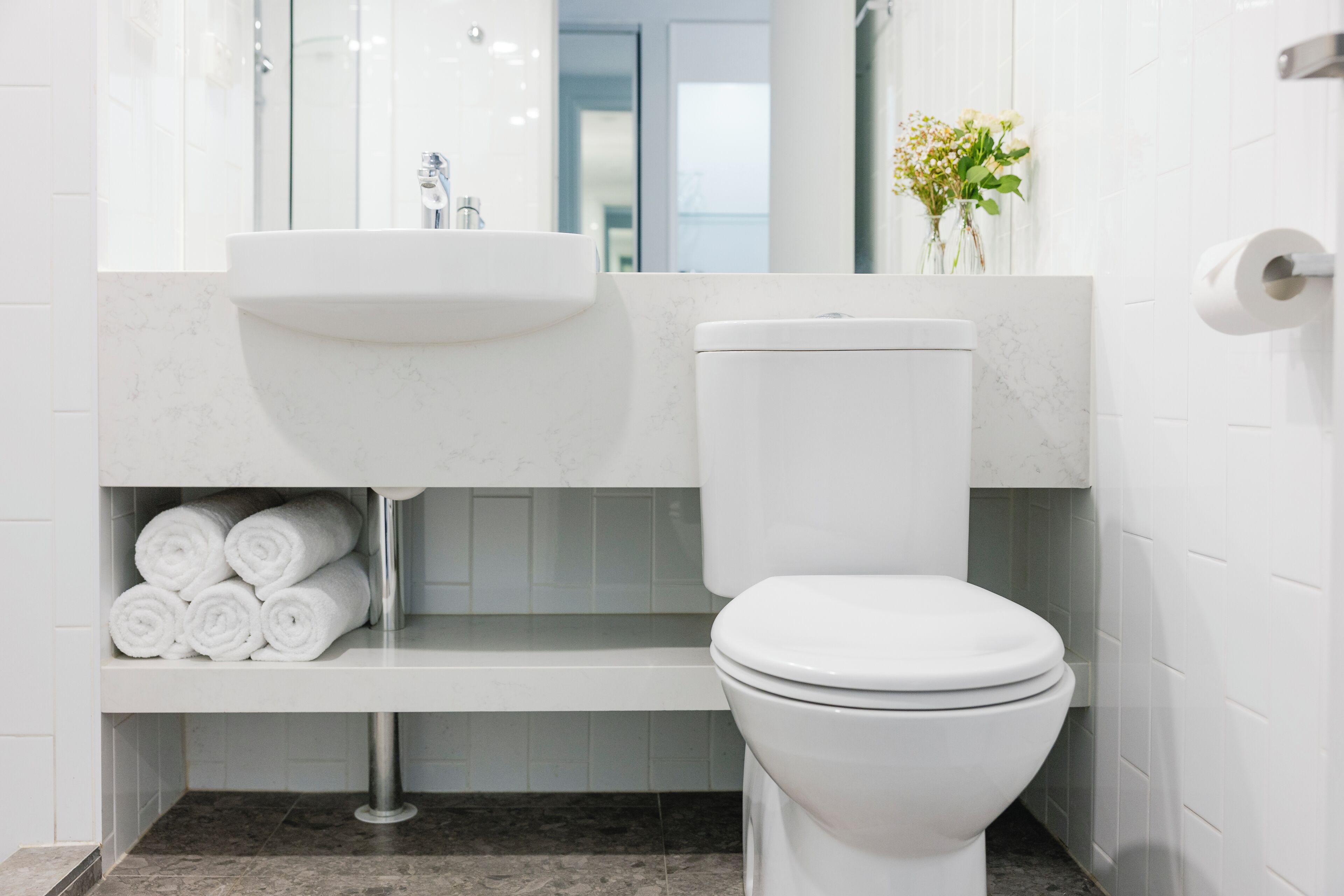 Casa de banho moderna com lavatório branco, sanita e bancada de mármore.