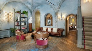 A spacious living room with a leather sofa, two wicker chairs, a bookshelf, and a decorative ceiling. - J And J Historic House Hotel (Florence)