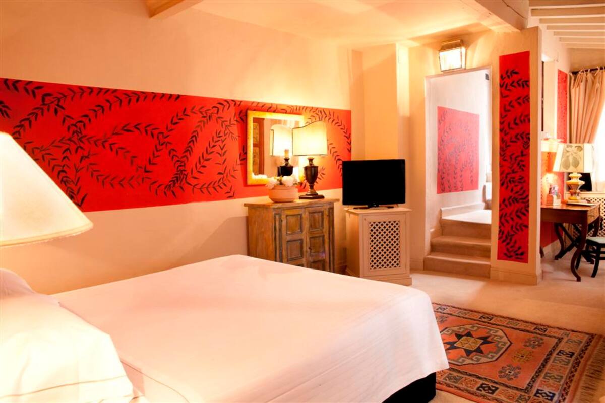 A hotel room with a bed, a television, a desk with a chair, a mirror, and a staircase.